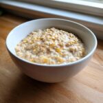 A close-up of creamy banana oatmeal topped with cinnamon in a white bowl on a wooden surface.