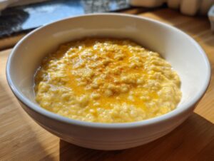 A close-up of creamy banana oatmeal in a white bowl, topped with melted butter or syrup and a sprinkle of cinnamon.