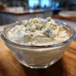 Close-up of a creamy, white blue cheese dip topped generously with chunks of blue cheese crumbles.