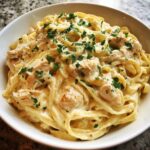 A close-up of rich, creamy chicken fettuccine alfredo topped with fresh parsley and grated cheese.