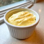 A close-up of thick, creamy, yellow homemade garlic aioli served in a small white fluted ramekin.