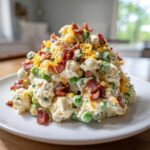 A generous mound of creamy pea salad mixed with bacon bits and topped with shredded cheddar cheese.