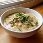 A close-up of a creamy white chicken chili bowl, topped with shredded white chicken and fresh cilantro.