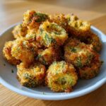 A close-up of a mound of perfectly golden and crispy fried okra pieces served on a light gray plate.