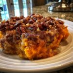 A close-up serving of rich, orange crockpot sweet potato casserole topped with a crunchy pecan streusel.