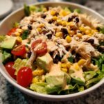 A vibrant bowl of southwest chicken salad featuring shredded chicken, black beans, corn, avocado, and cherry tomatoes drizzled with creamy dressing.