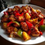 Close-up of glazed, browned chicken pieces mixed with pineapple chunks and red and green bell peppers from the hawaiian chicken sheet pan.