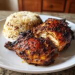 Close-up of perfectly cooked Jamaican Jerk Chicken pieces served with a mound of rice and peas.