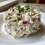A close-up of a perfectly molded portion of greek yogurt chicken salad, topped with fresh parsley.