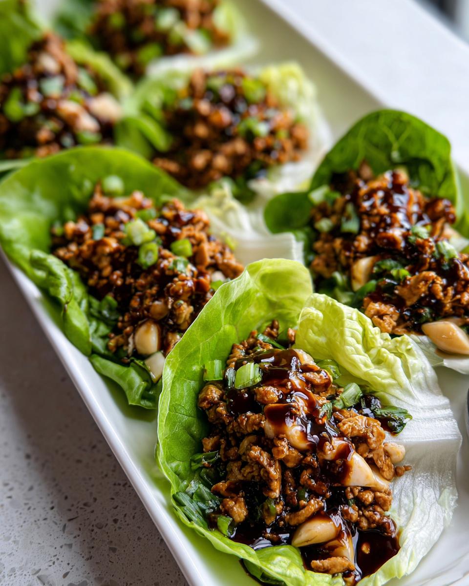Close-up of several delicious chicken lettuce wraps filled with savory ground chicken mixture, topped with green onions and a dark sauce.