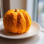 A bright orange pumpkin cheese ball shaped like a small pumpkin, sitting on a white plate.