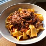 Close-up of a bowl of wide egg noodles topped generously with rich, shredded beef ragu sauce.
