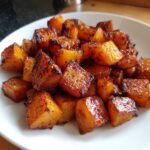 Close-up of perfectly caramelized and glazed roasted butternut squash cubes served on a white plate.