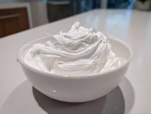 A white bowl filled with stiff, glossy, perfectly whipped royal icing recipe, ready for decorating.