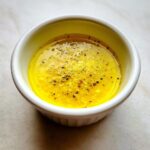 Close-up of bright yellow homemade salad dressing seasoned with cracked black pepper in a white ramekin.