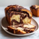 A close-up of a freshly baked chocolate babka loaf, with one slice cut and resting in front, showing the beautiful chocolate swirls.