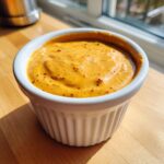 Close-up of creamy, orange-hued smash burger sauce speckled with spices in a white ramekin.