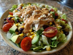 A vibrant bowl of southwest chicken salad featuring shredded chicken, avocado, tomatoes, corn, black beans, and a creamy dressing.