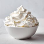 A white bowl filled with stiff, perfectly piped white topping, resembling the texture needed for a royal icing recipe.