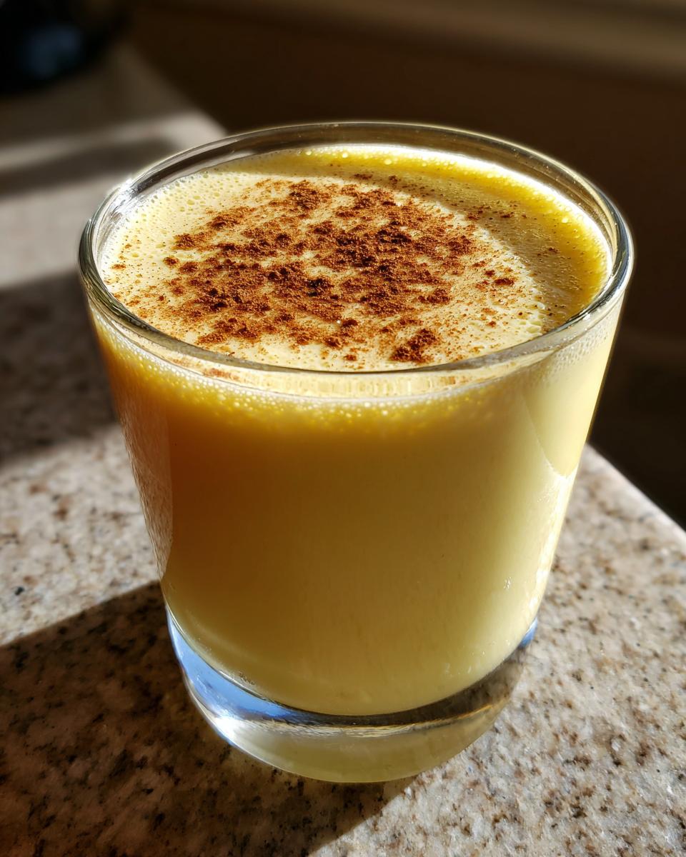 Close-up of a glass filled with thick, yellow eggnog, topped with a dusting of cinnamon.