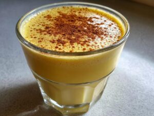 Close-up of a glass filled with thick, creamy yellow eggnog, topped generously with ground cinnamon.