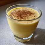 Close-up of a glass filled with thick, creamy, yellow eggnog, freshly dusted with cinnamon.