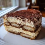A delicious slice of layered tiramisu cheesecake dusted heavily with cocoa powder.