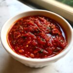Close-up of rich, chunky homemade pizza sauce in a small white bowl, ready for use.