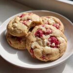 A stack of soft, chewy white chocolate raspberry cookies on a small white plate, one cookie has a bite taken out.